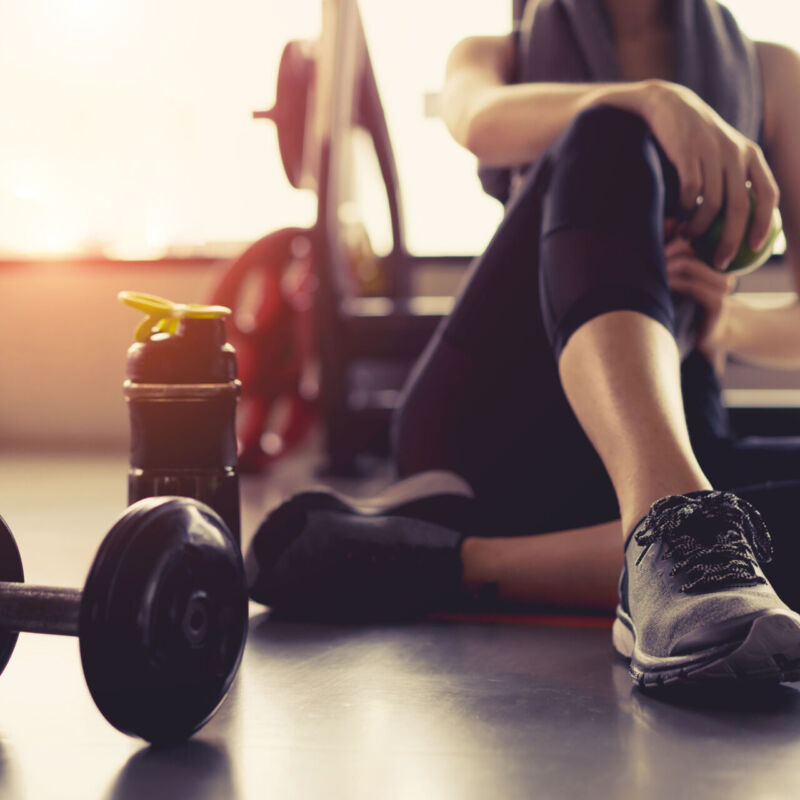 Woman exercise workout in gym fitness breaking relax holding apple fruit after training sport with dumbbell and protein shake bottle healthy lifestyle bodybuilding.