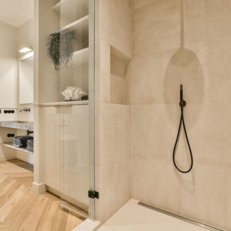 a modern bathroom with wood flooring and beige tiles on the walls, along with a walk - in shower